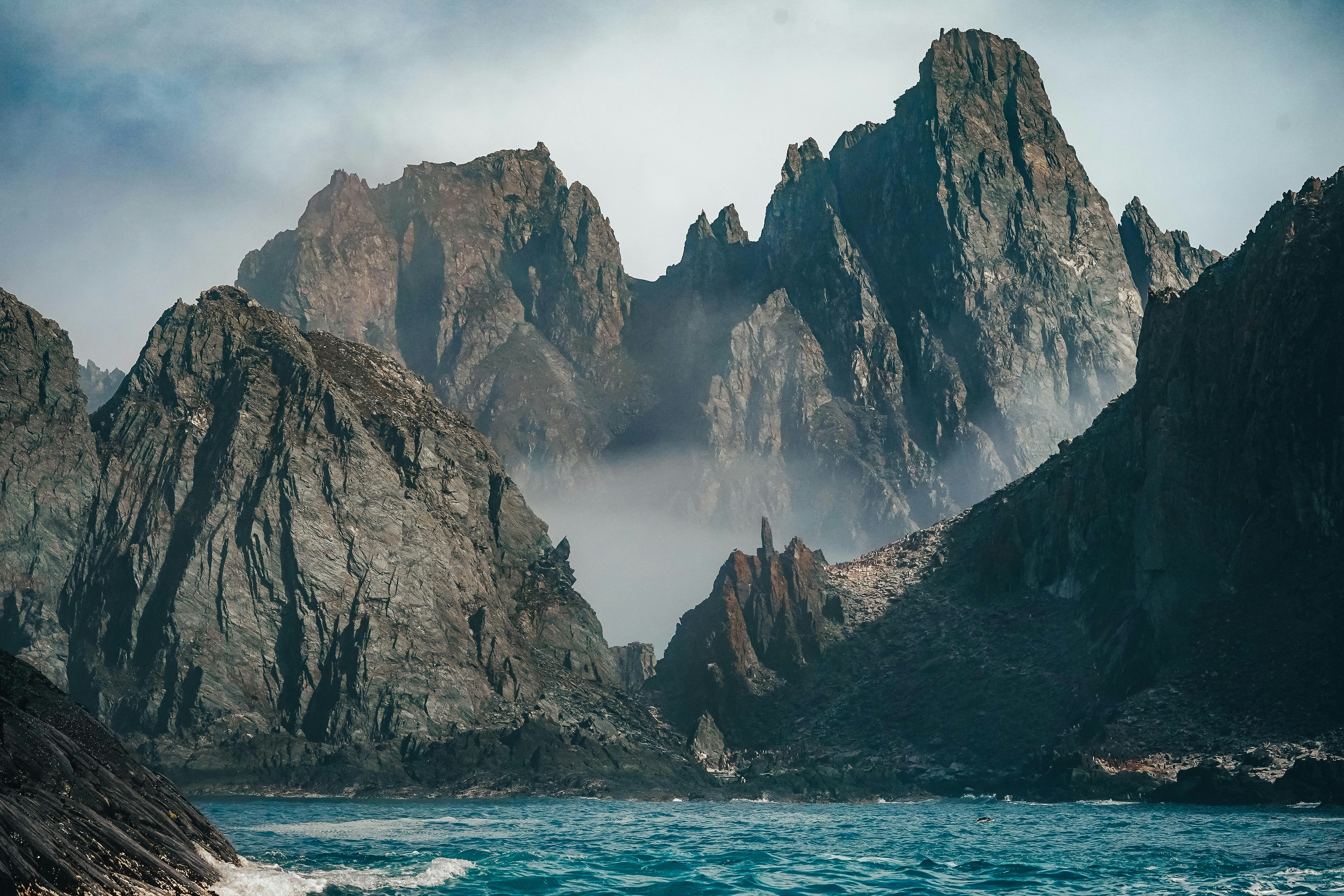 brown rocky mountain beside blue sea under white sky during daytime